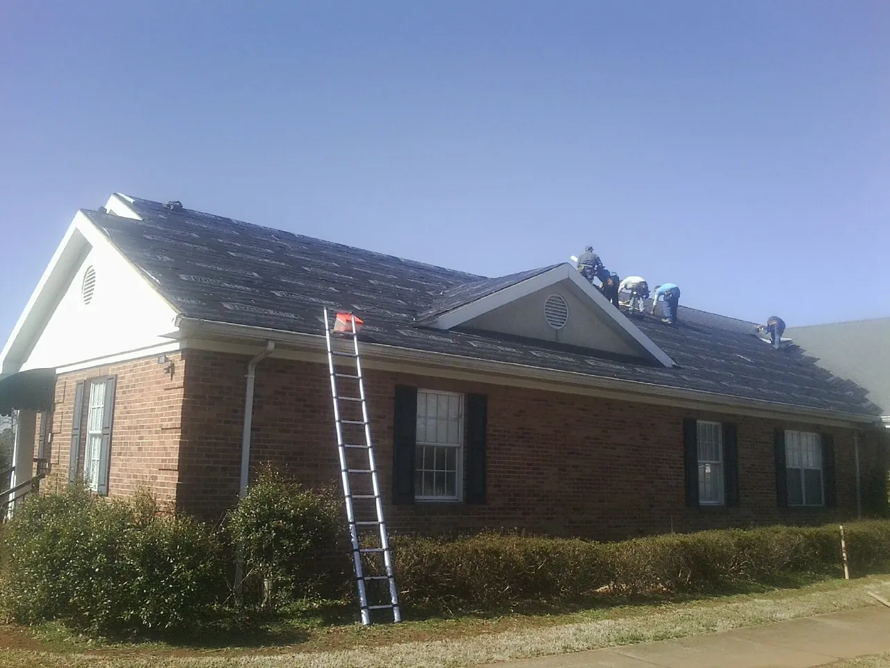 Crew tearing shingles off a brick ranch roof with a ladder set — Emergency Roof Repair work by our crew in Taylor