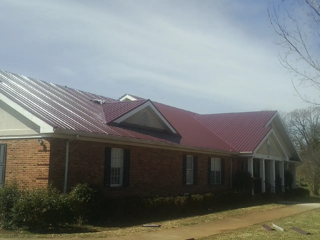 Red metal roof with gabled entries on a long brick building, from a Hail Damage Roof Repair job in Taylor