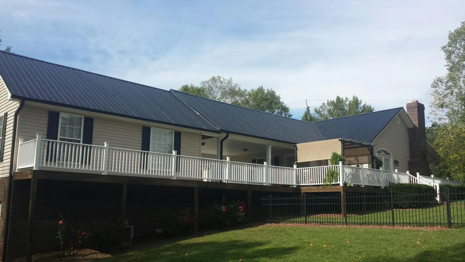 Black metal roof above a long white railed deck on a hillside home in Taylor